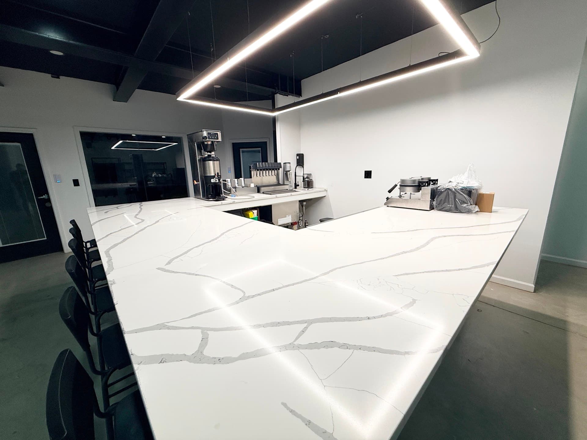 A long white marble counter with a coffee machine and bar stools, lit by a linear ceiling light.