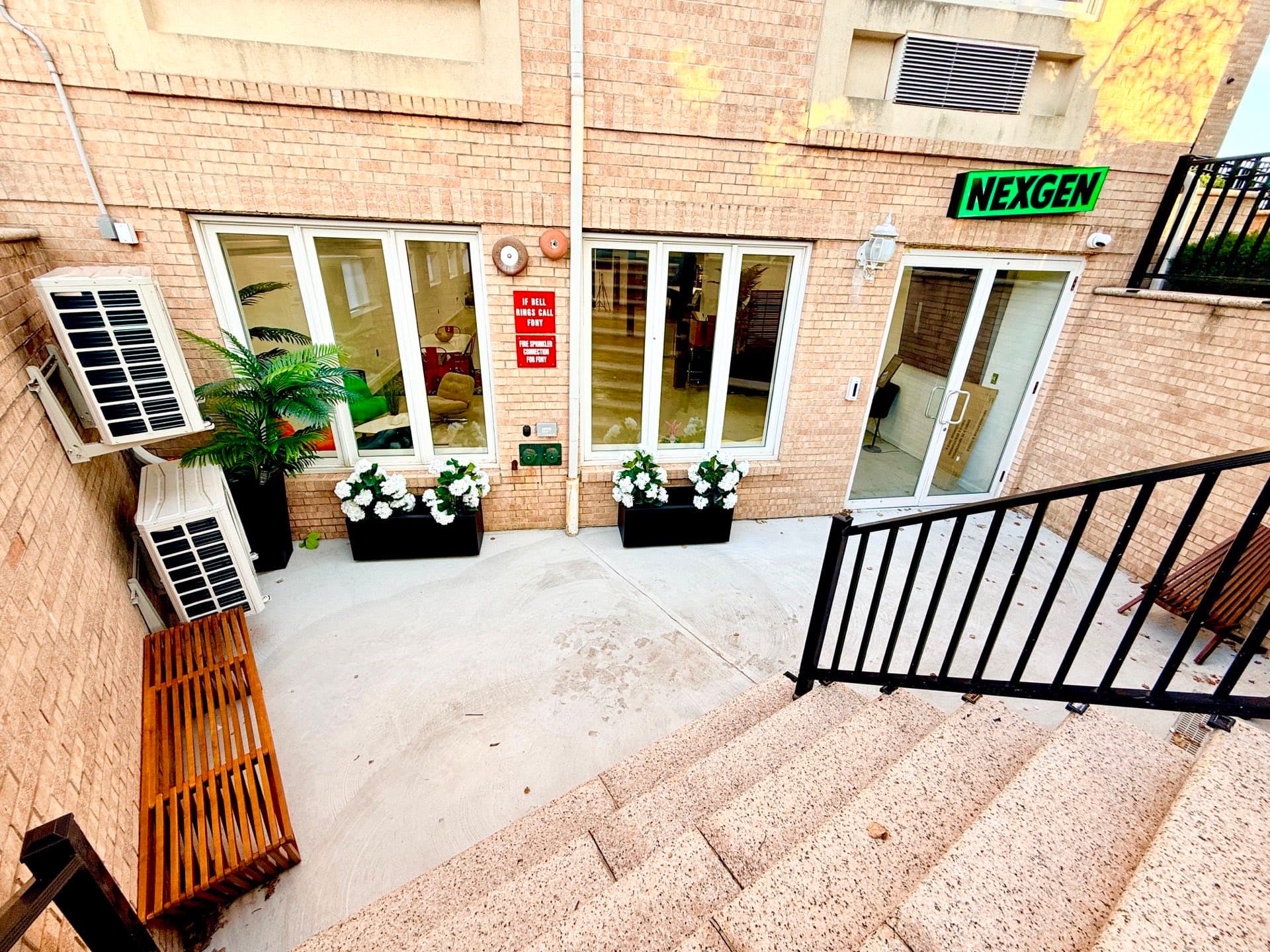 The entrance to 6 Arc Place seen from above: a short flight of steps down to a paved forecourt with planters of white flowers, leading to tall glass doors set into a brick wall.