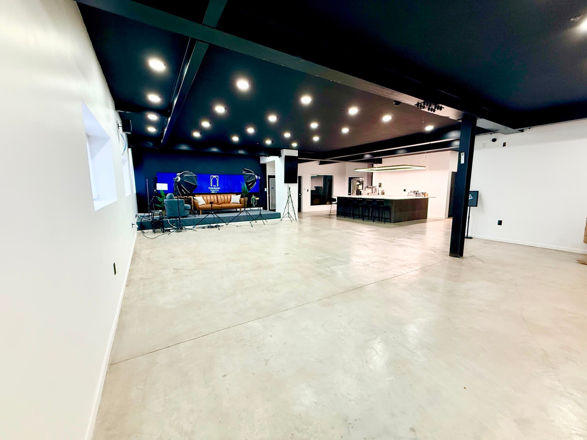 The main hall at 6 Arc Place: a wide polished-concrete floor under a black ceiling, with a low stage at one end and the café counter at the other.