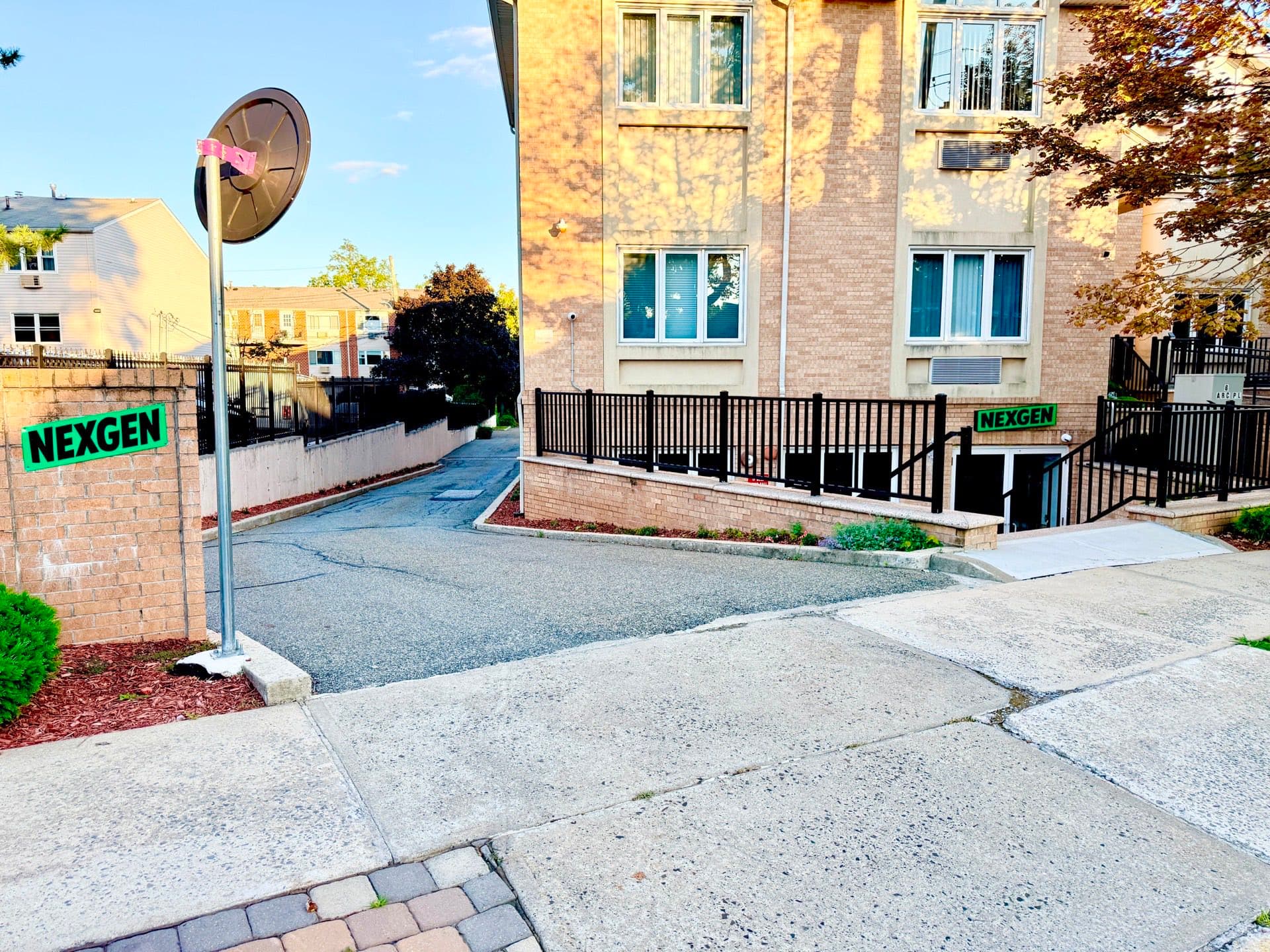 The street outside 6 Arc Place: a paved driveway running down between brick apartment buildings, with railings on the right and a traffic mirror on a pole at the corner.